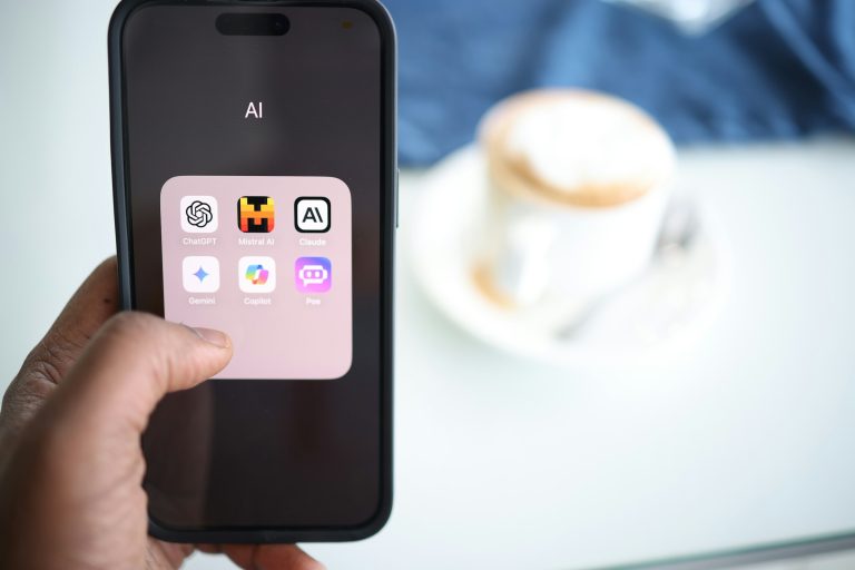 man holding a phone open to a folder of AI tools like ChatGPT Gemini and Claude with a cup of coffee and desk in the background — the shift from search to query intent online